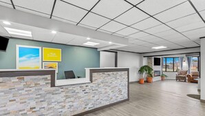A reception area with a stone-textured counter, a 'Hello Sunshine' sign, and a view through a glass door to an outdoor seating area. - Days Inn by Wyndham Alpena (Alpena)