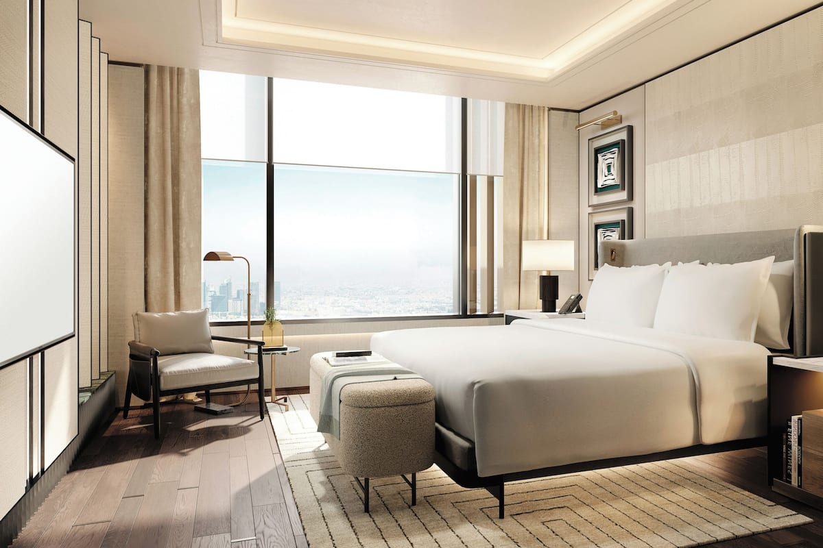 Een hotelkamer met een groot bed, een bureau, een stoel, een klein tafeltje, een lamp en uitzicht op de stad.
