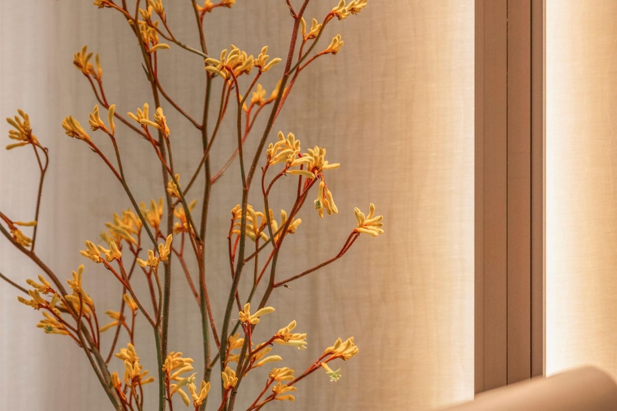 A vase with yellow flowers on a table next to a lamp.