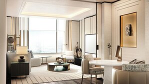 A modern hotel room with a large window, a round coffee table, a sofa, a dining table, and a decorative vase.