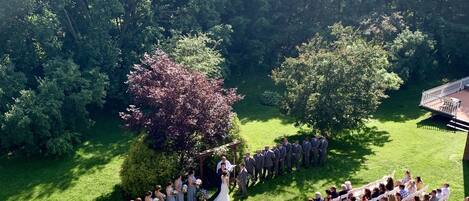 An outdoor wedding ceremony with guests seated on white chairs arranged in rows.