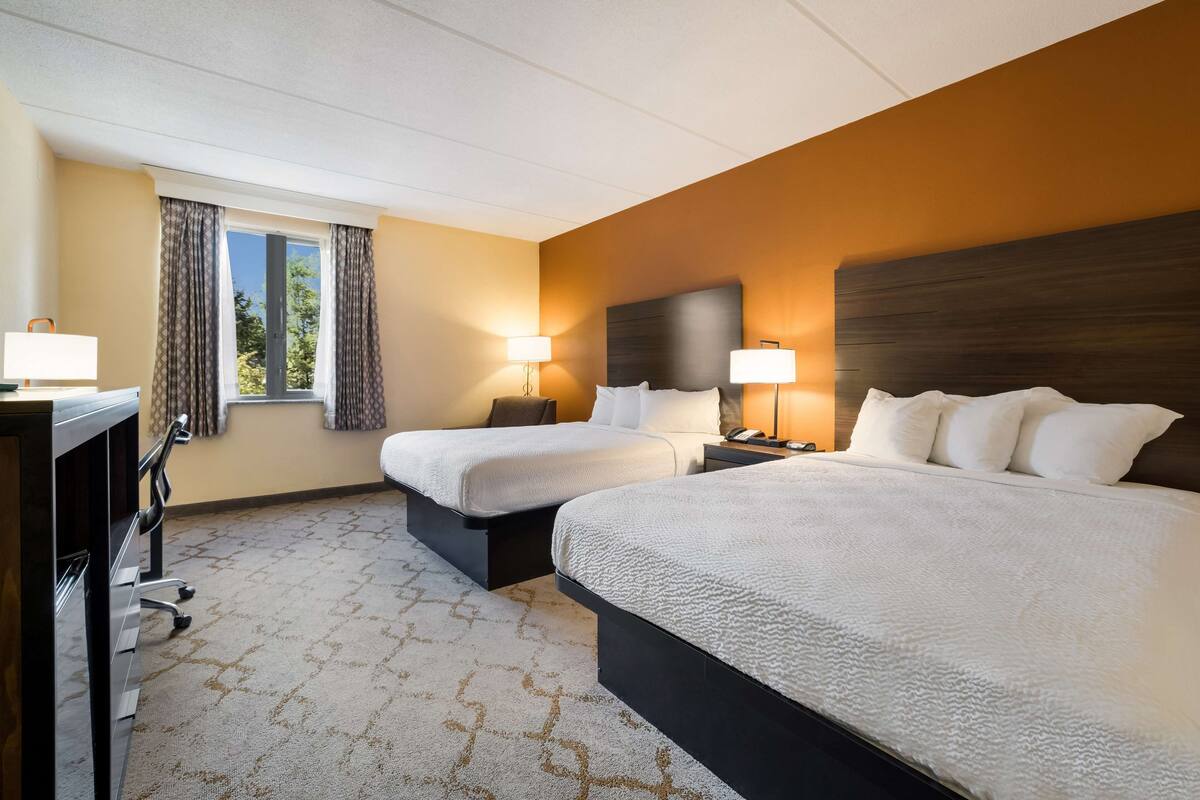 A hotel room with two beds, a desk, and a window with curtains.