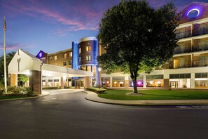 Hotel stands amidst a manicured lawn, marked by a well-lit entrance and a flagpole.