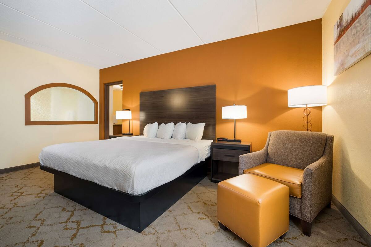 A hotel room with a large bed, a chair, a nightstand, and a lamp.