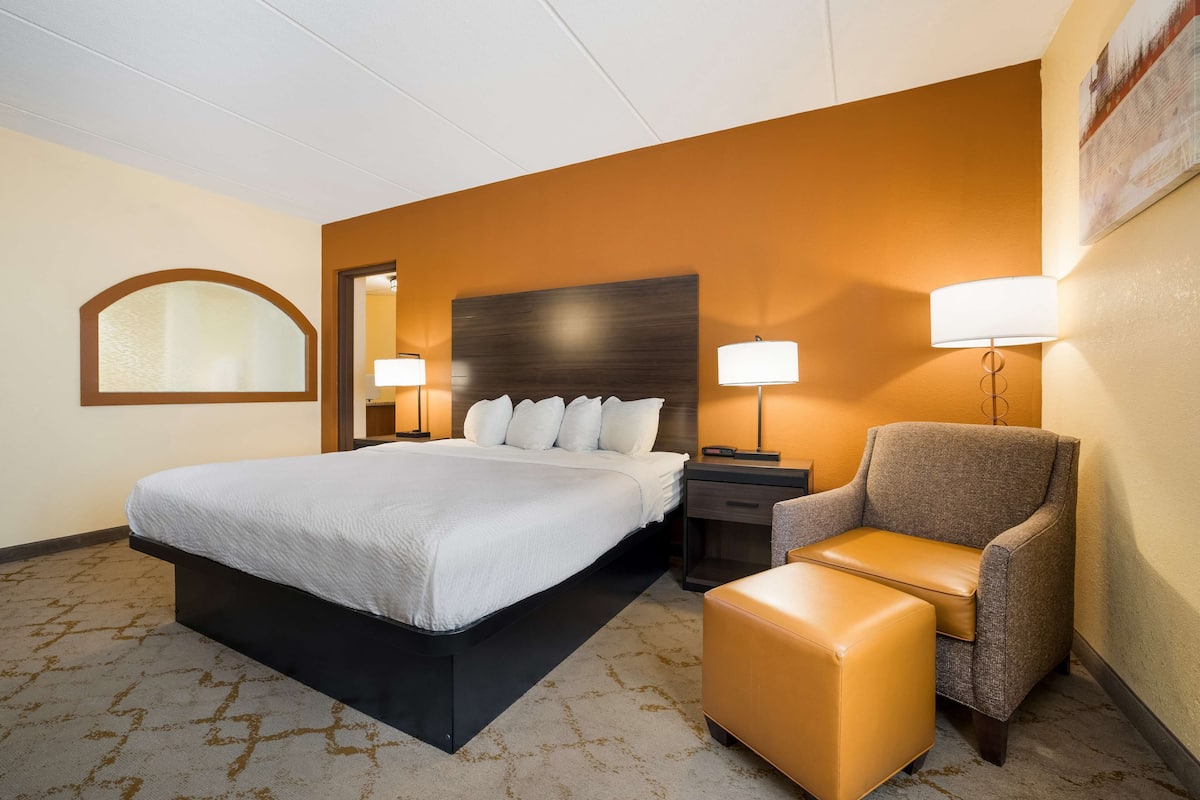 A hotel room with a large bed, a chair, a nightstand, and a lamp.