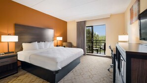 Quarto de hotel com uma cama grande, duas luminárias de cabeceira, uma mesa com televisão e uma varanda com vista.