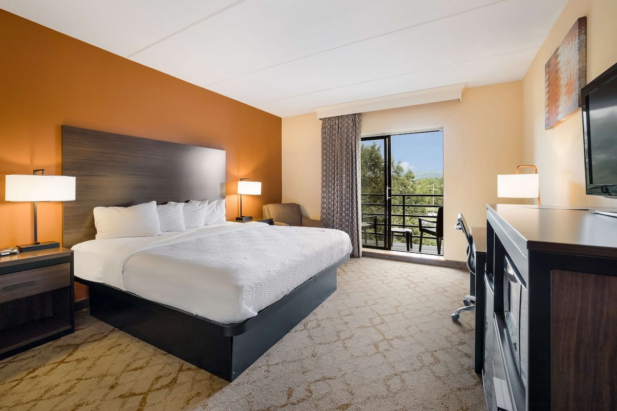 A hotel room with a large bed, two bedside lamps, a desk with a TV, and a balcony with a view.