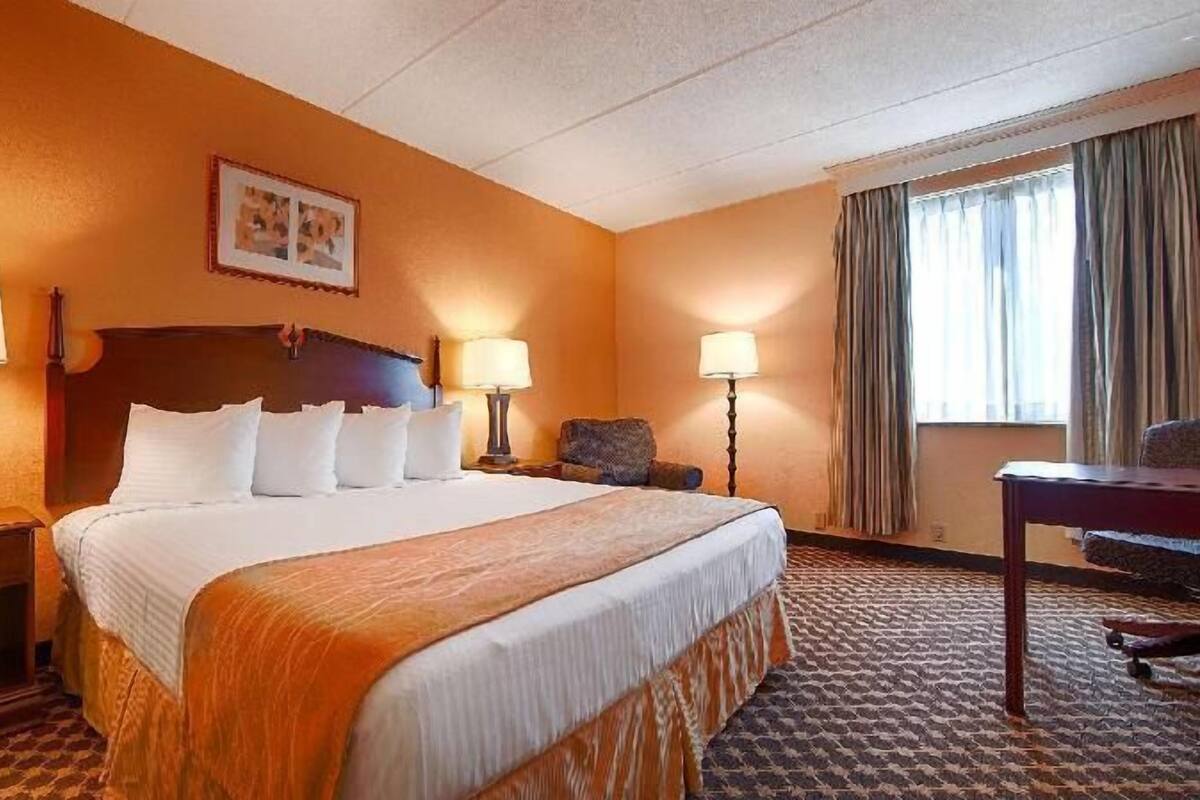 A hotel room with a large bed, two bedside tables with lamps, a chair, a desk, and a window with curtains.