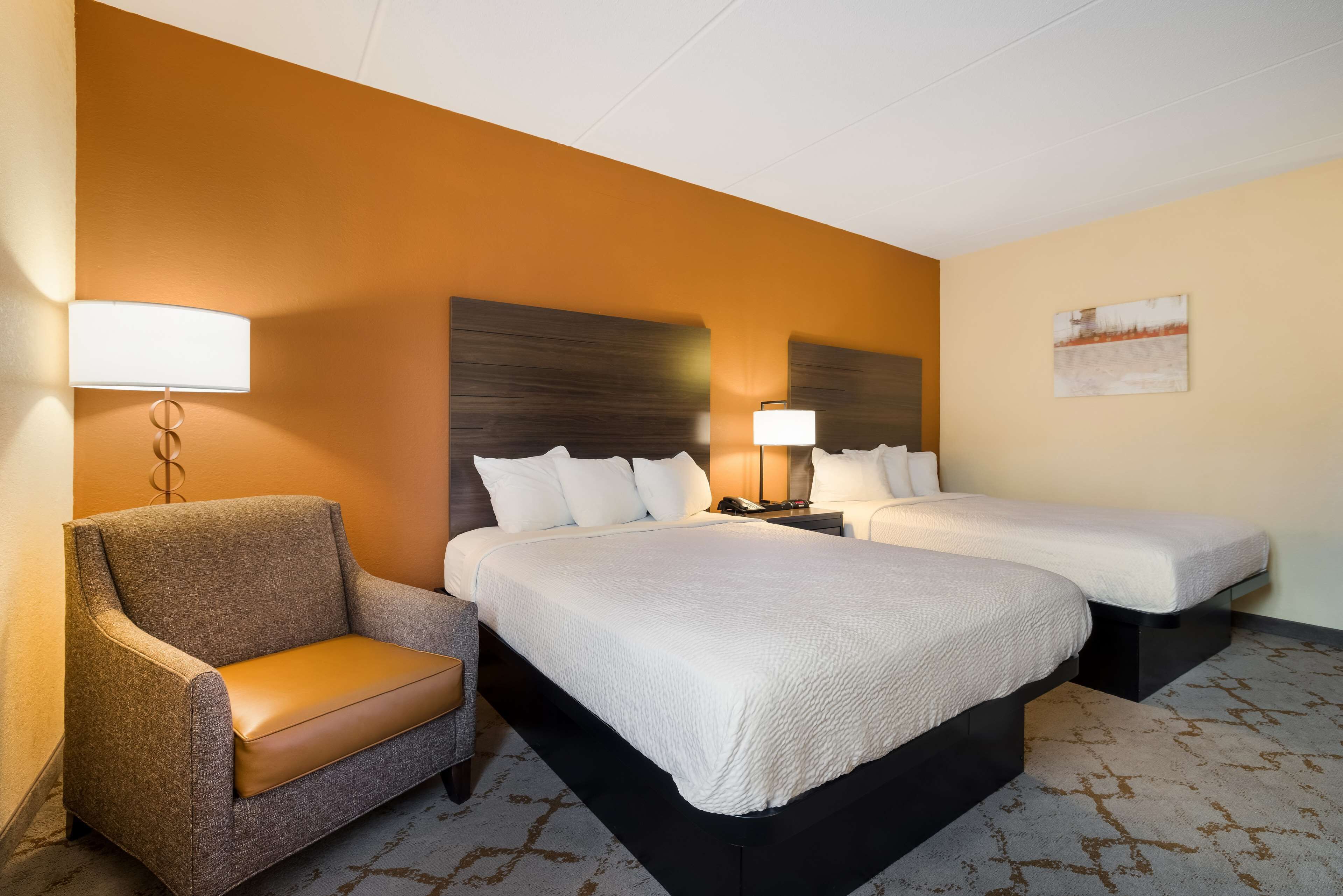 A hotel room with two beds, a sofa, a lamp, and a painting on the wall.