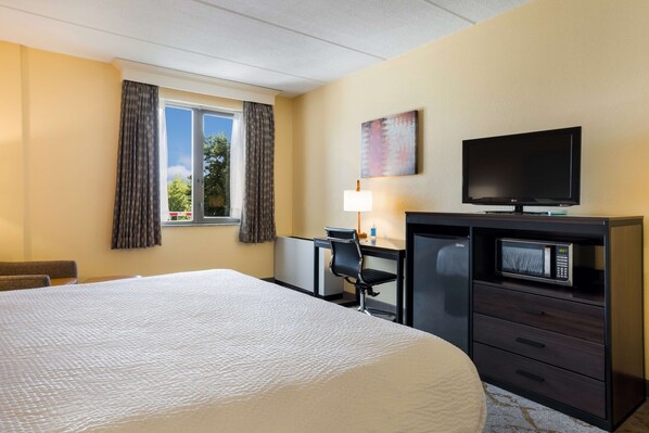 A hotel room with a large bed, a desk with a chair, a television, a microwave, and a window with curtains.