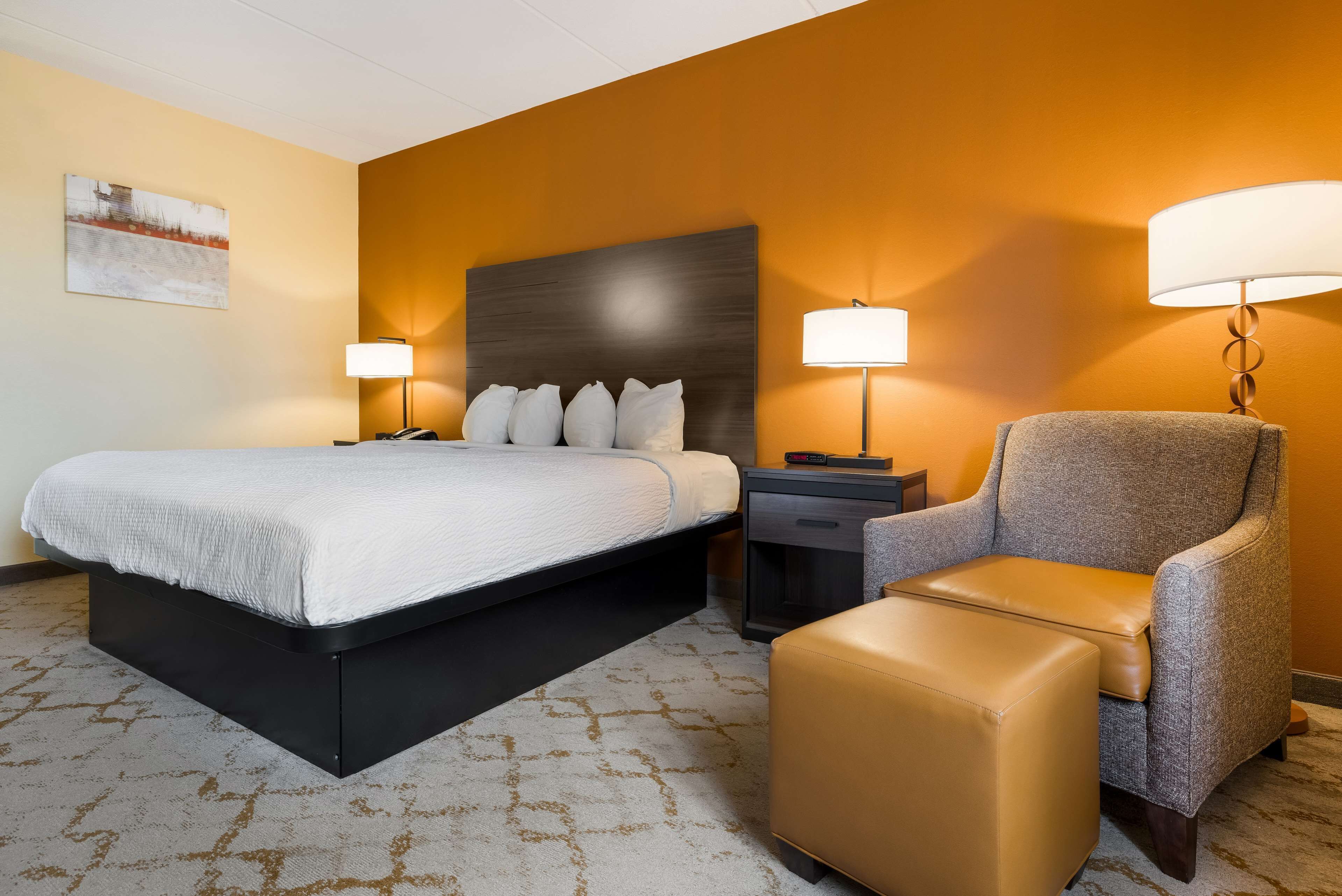 A hotel room with a large bed, a chair, a nightstand, and two wall-mounted lamps.
