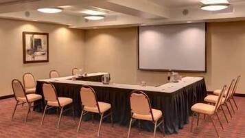 A conference room with a long table, chairs, a projector screen, and a carpeted floor.
