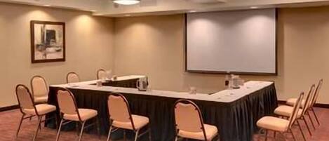 A conference room with a long table, chairs, a projector screen, and a carpeted floor.
