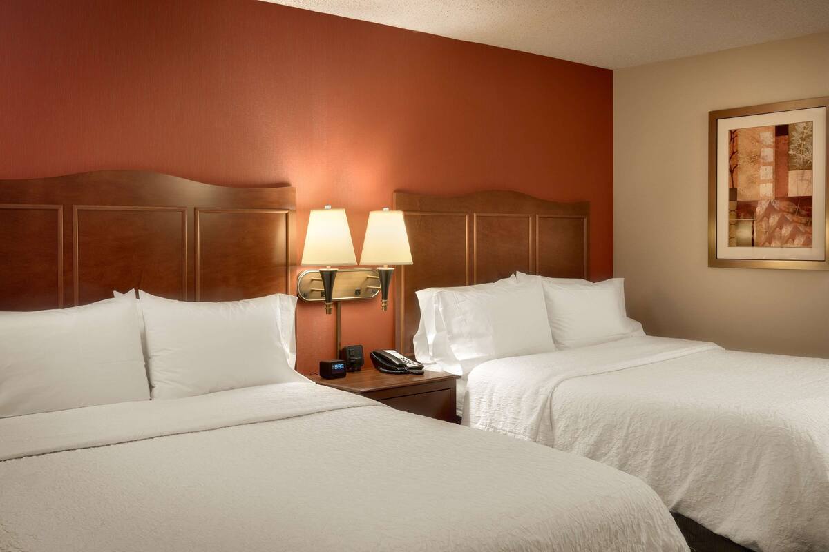 A hotel room with two beds, a nightstand with a lamp, a phone, and a painting on the wall.