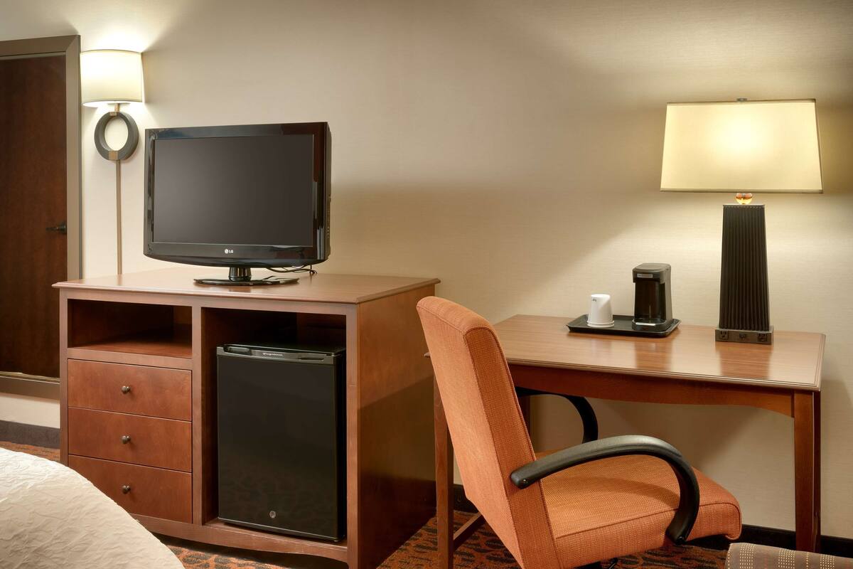 A hotel room with a wooden desk, a television, a coffee maker, and a chair.