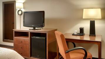 A hotel room with a wooden desk, a television, a coffee maker, and a chair.