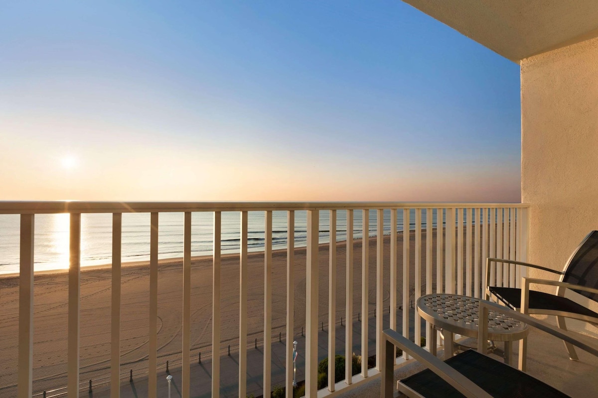 A balcony with a view of the beach and ocean during sunset.