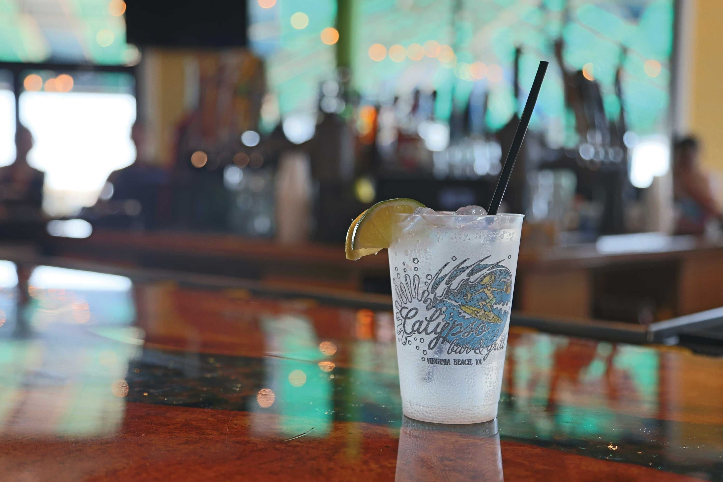 Um bar com uma bebida em copo transparente, um canudo e uma fatia de limão.