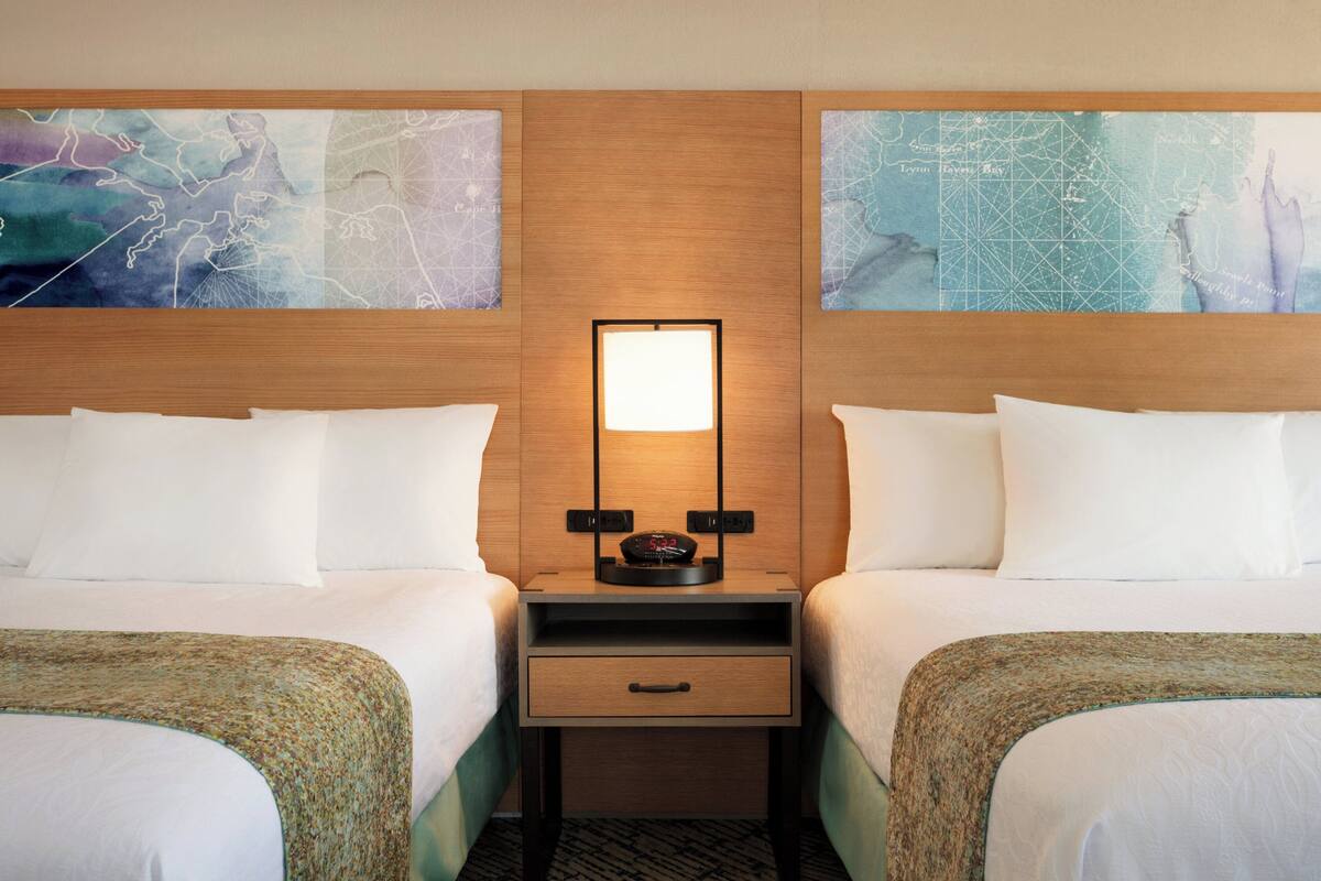 A hotel room with two beds, a nightstand with a clock, and abstract wall art.