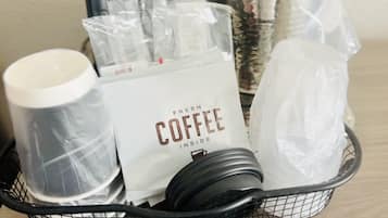 A basket containing a coffee maker, a container of fresh coffee, a candle, and a glass jar.