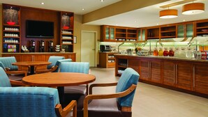 Um lobby moderno de hotel com mobiliário de madeira, área de bar e uma televisão na parede.