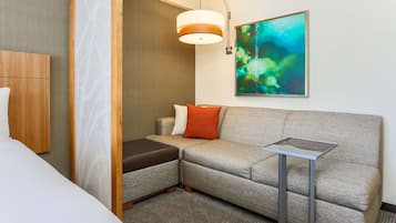 A modern hotel room with a sofa, a small table, a painting, and a bed.