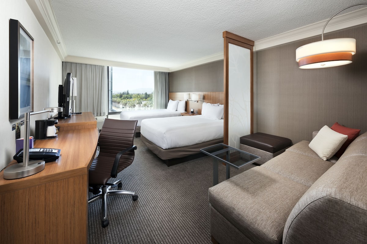Ett hotellrum med en säng, ett skrivbord med en dator, en stol, en soffa och ett stort fönster med utsikt.