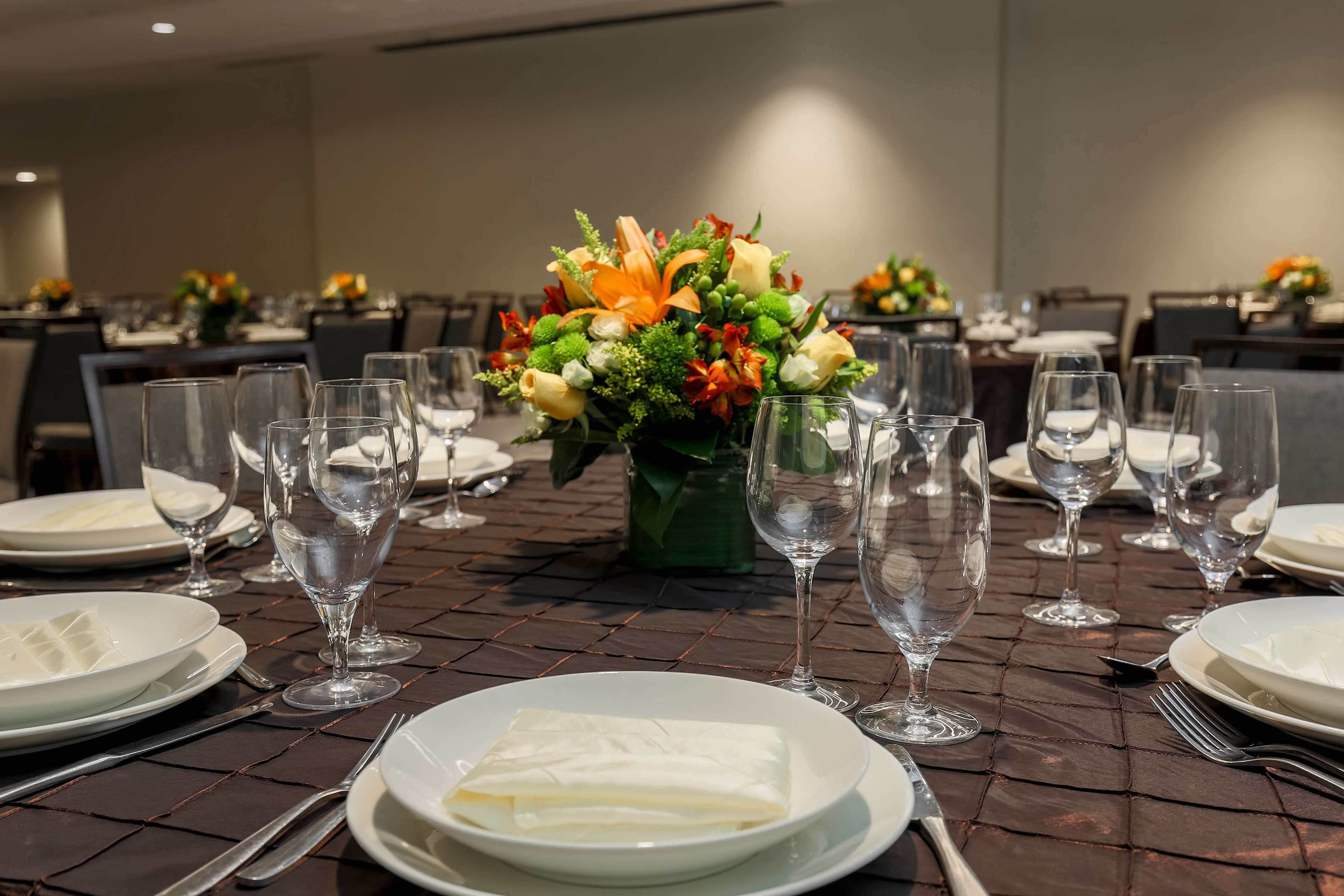A dining table set with plates, cutlery, and wine glasses, with a centerpiece of flowers.