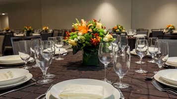 A dining table set with plates, cutlery, and wine glasses, with a centerpiece of flowers.
