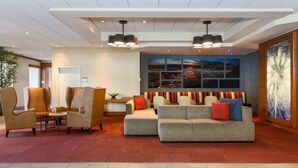 Um lobby moderno com áreas de estar, uma grande janela com vista para a cidade e um painel decorativo na parede.