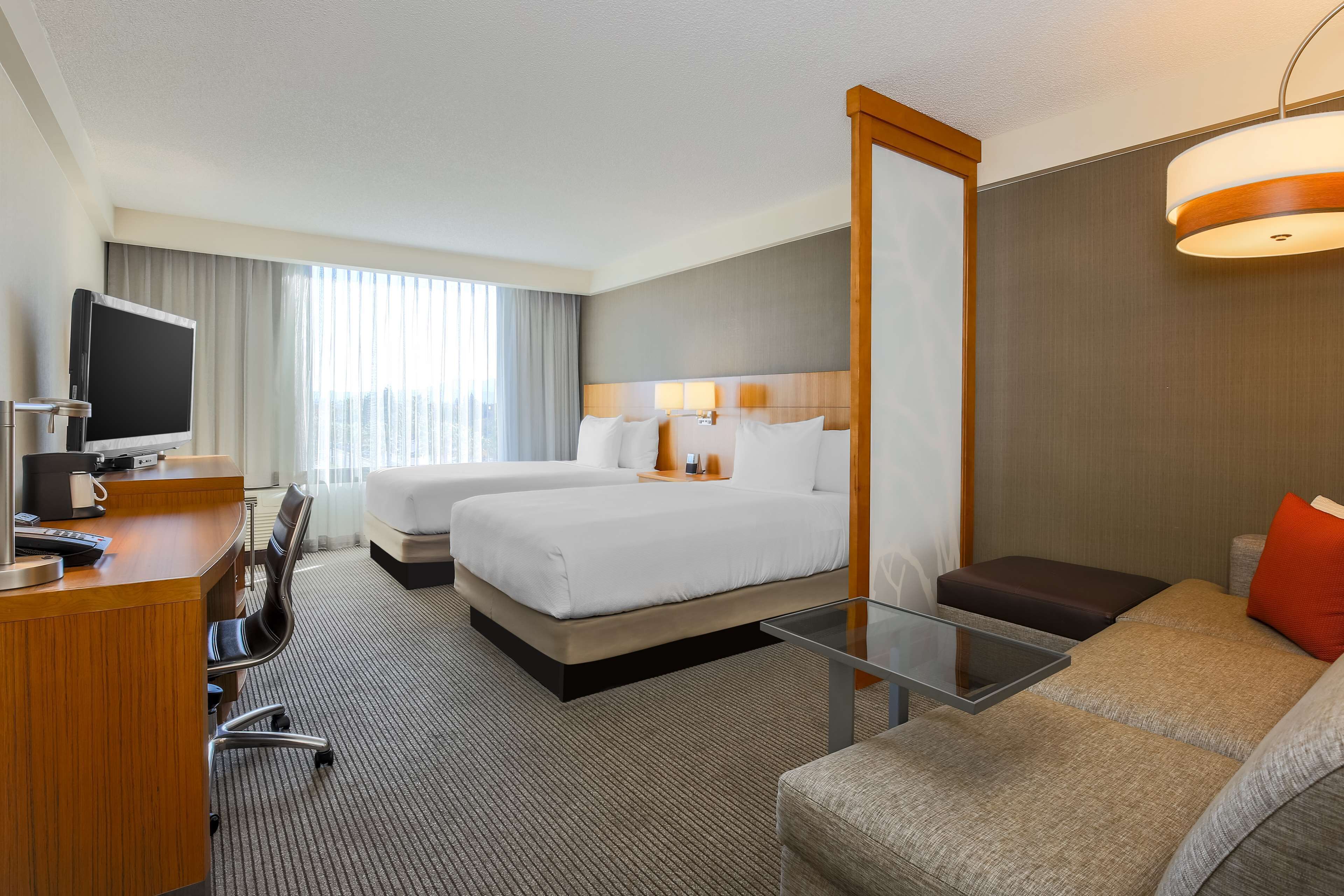 Une chambre d’hôtel équipée d’un bureau, de deux lits, d’un canapé, d’une télévision et d’un grand miroir.