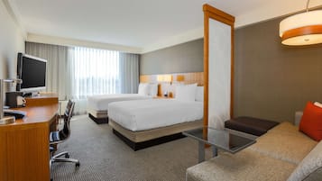 Une chambre d’hôtel équipée d’un bureau, de deux lits, d’un canapé, d’une télévision et d’un grand miroir.