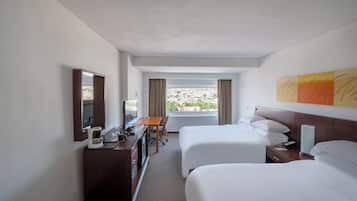 Une chambre d’hôtel avec deux lits, un bureau avec une chaise, une commode, un miroir, une fenêtre avec des rideaux et un tableau au mur.