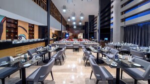 Un comedor moderno con varias mesas y sillas, un área de asientos central y una cocina visible al fondo.