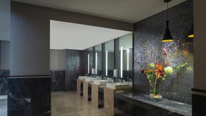 Un baño moderno con suelo de mármol, varios lavamanos y una pared decorativa con mosaicos.