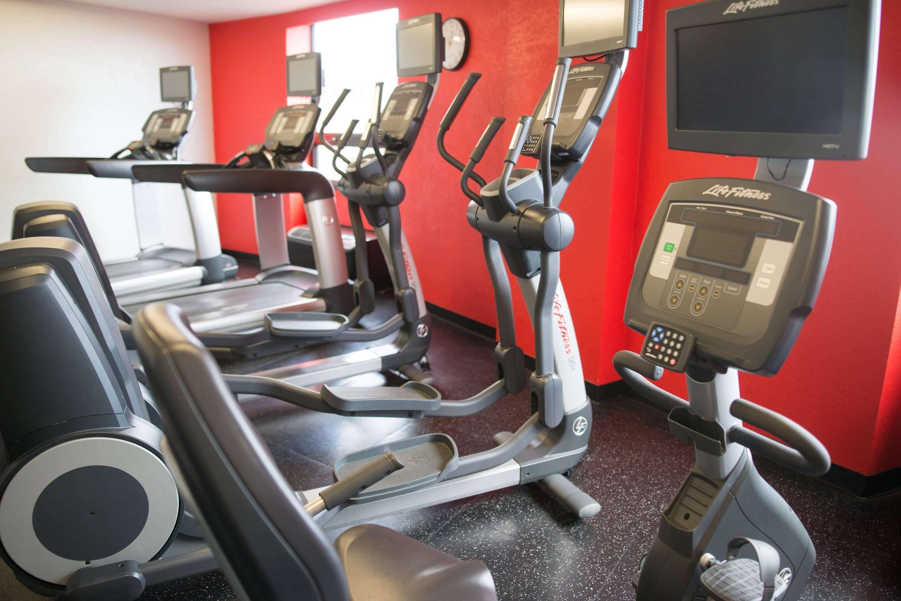 A gym with multiple elliptical machines and a treadmill, red walls, and a Life Fitness cardio machine.