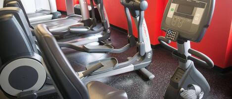 A gym with multiple elliptical machines and a treadmill, red walls, and a Life Fitness cardio machine.