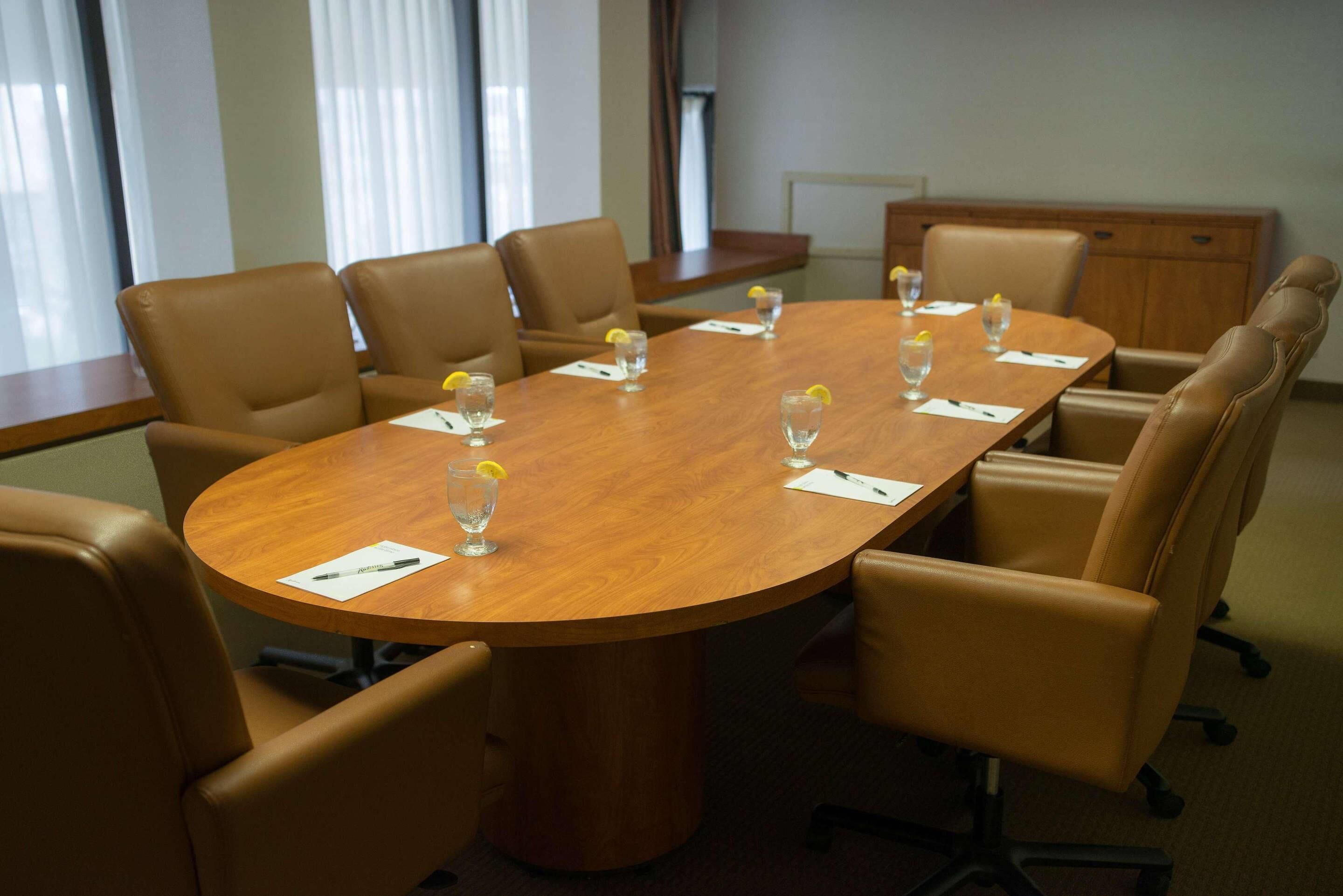 A conference room with a wooden table, brown leather chairs, and small glasses with lemon slices.