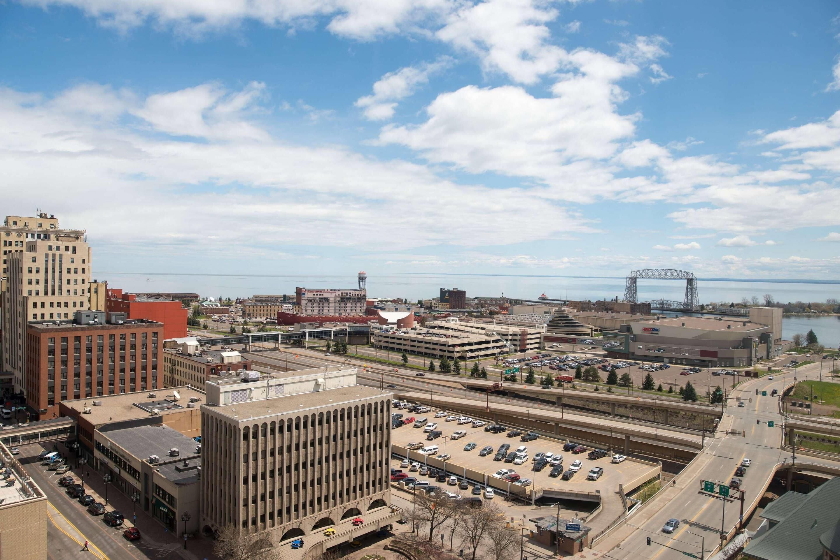 A cityscape with a parking lot, buildings, and a bridge in the background.