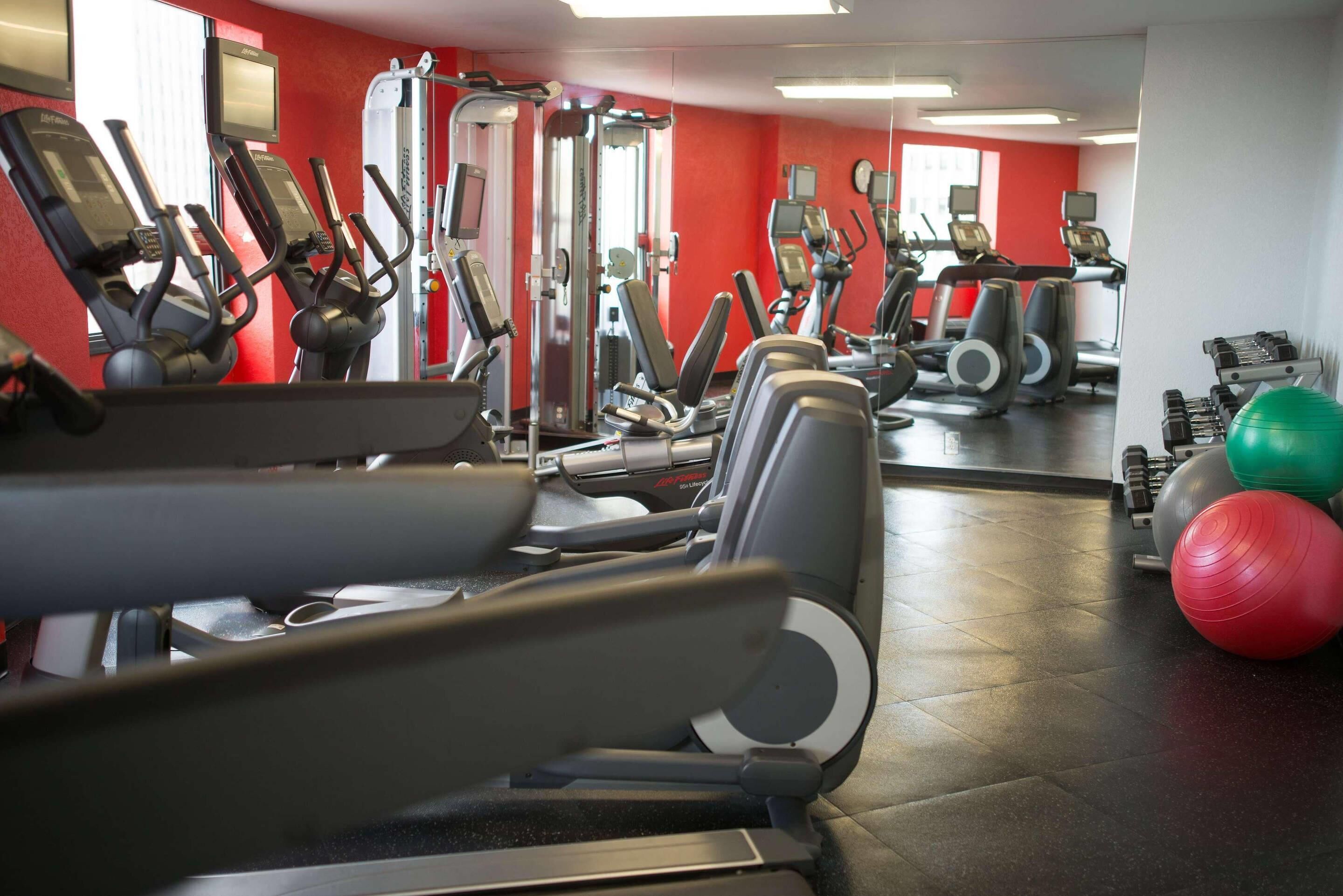 Une salle de sport équipée de divers appareils d’exercice, notamment des tapis de course et des appareils de musculation, ainsi que des ballons d’exercice.