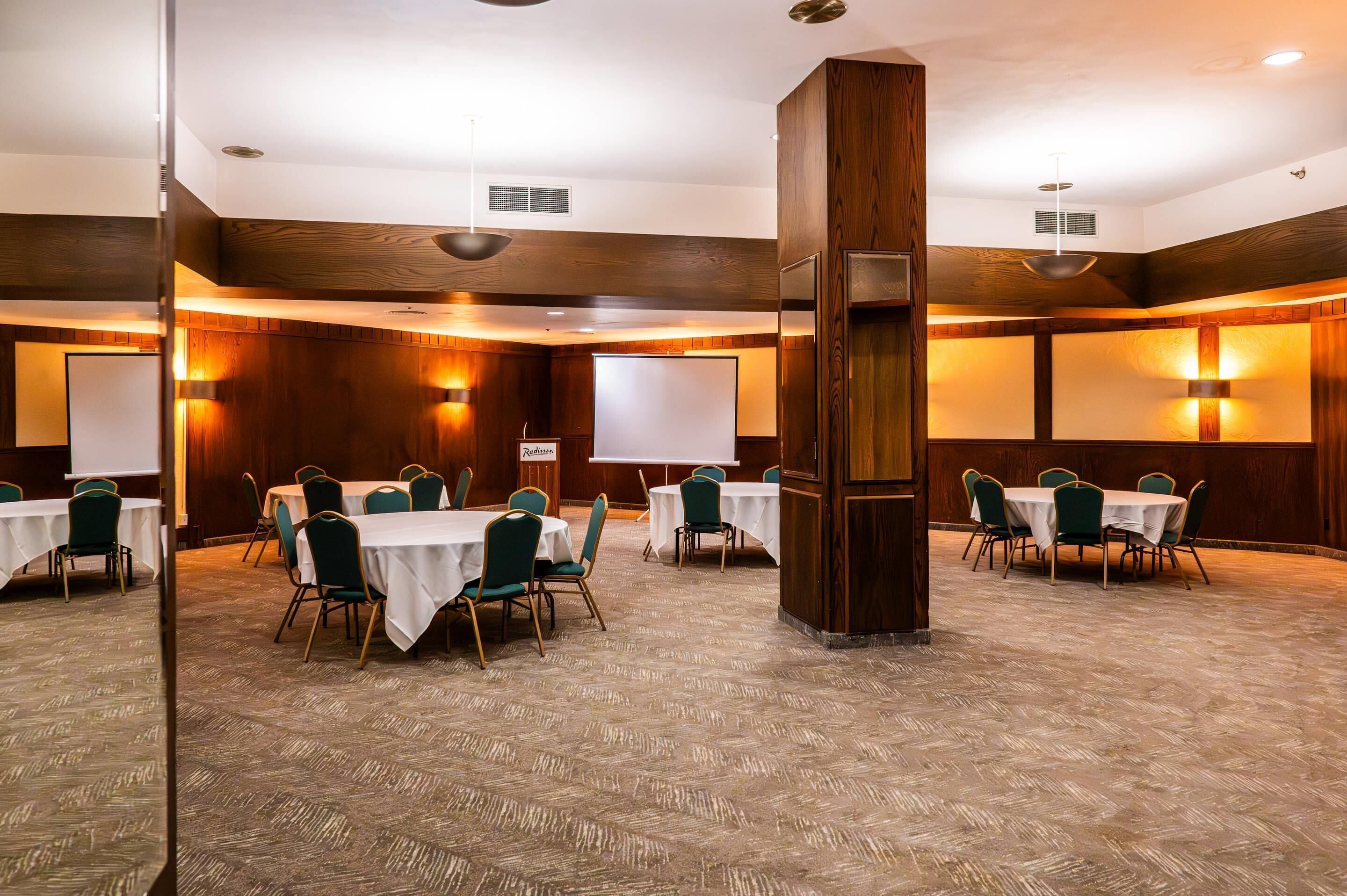 A conference room with multiple tables and chairs, a large pillar, and a whiteboard.
