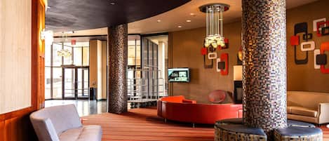 A lobby with a red carpet, a grey sofa, a red circular seating area, and a mosaic pillar.