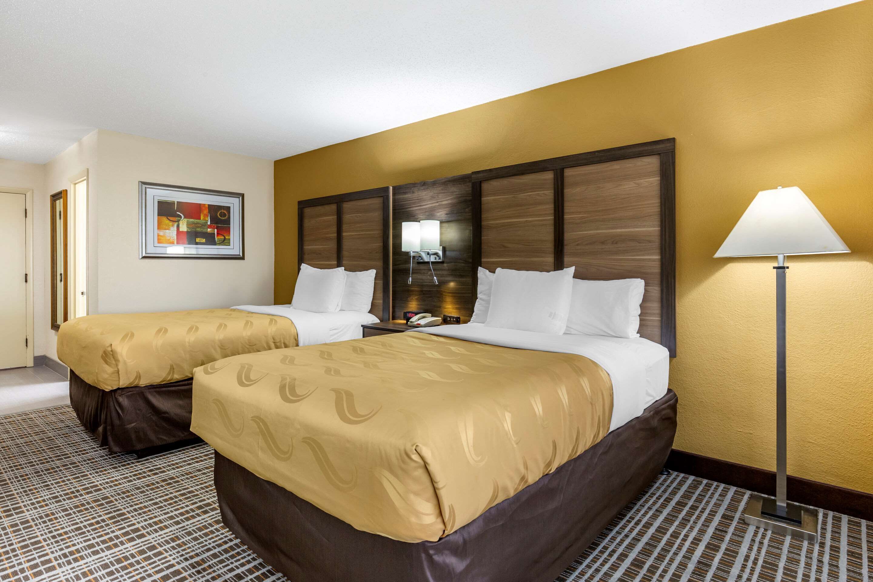 A hotel room with two beds, a large mirror, a lamp, and a framed artwork on the wall.