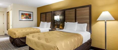 Habitación de hotel con dos camas, un espejo grande, una lámpara y una obra de arte enmarcada en la pared.