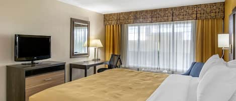 Habitación de hotel con cama, escritorio, televisión y ventana con cortinas.