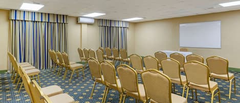 Une salle de conférence avec des rangées de chaises, un tableau blanc et une moquette à motifs.
