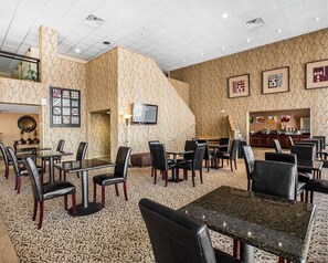 Welcome to our hotel lobby, featuring a central seating area with tables and chairs, a television, and a reception desk.