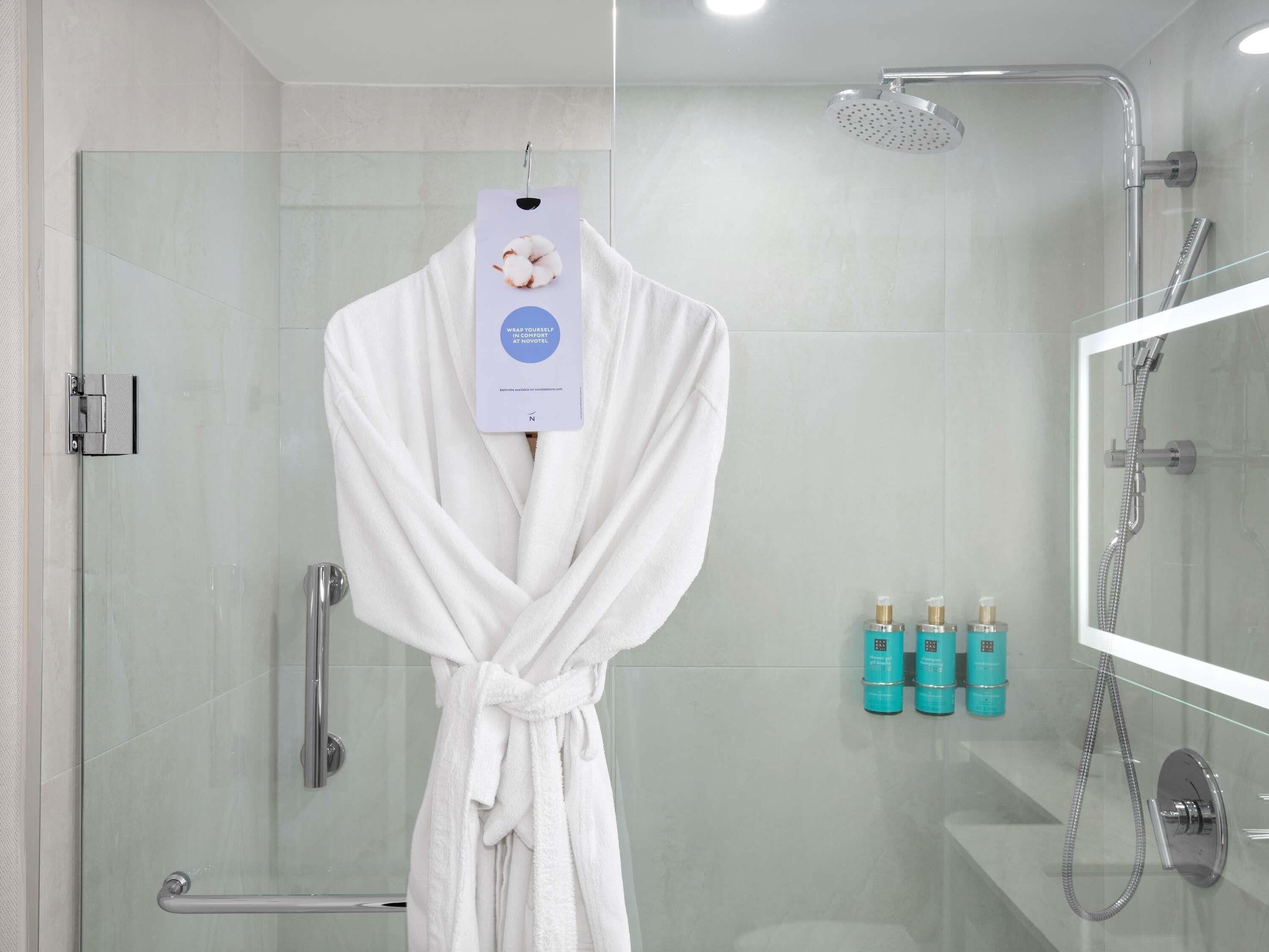 A glass-enclosed shower with a handheld showerhead, a glass door, and a towel rack with a white robe.