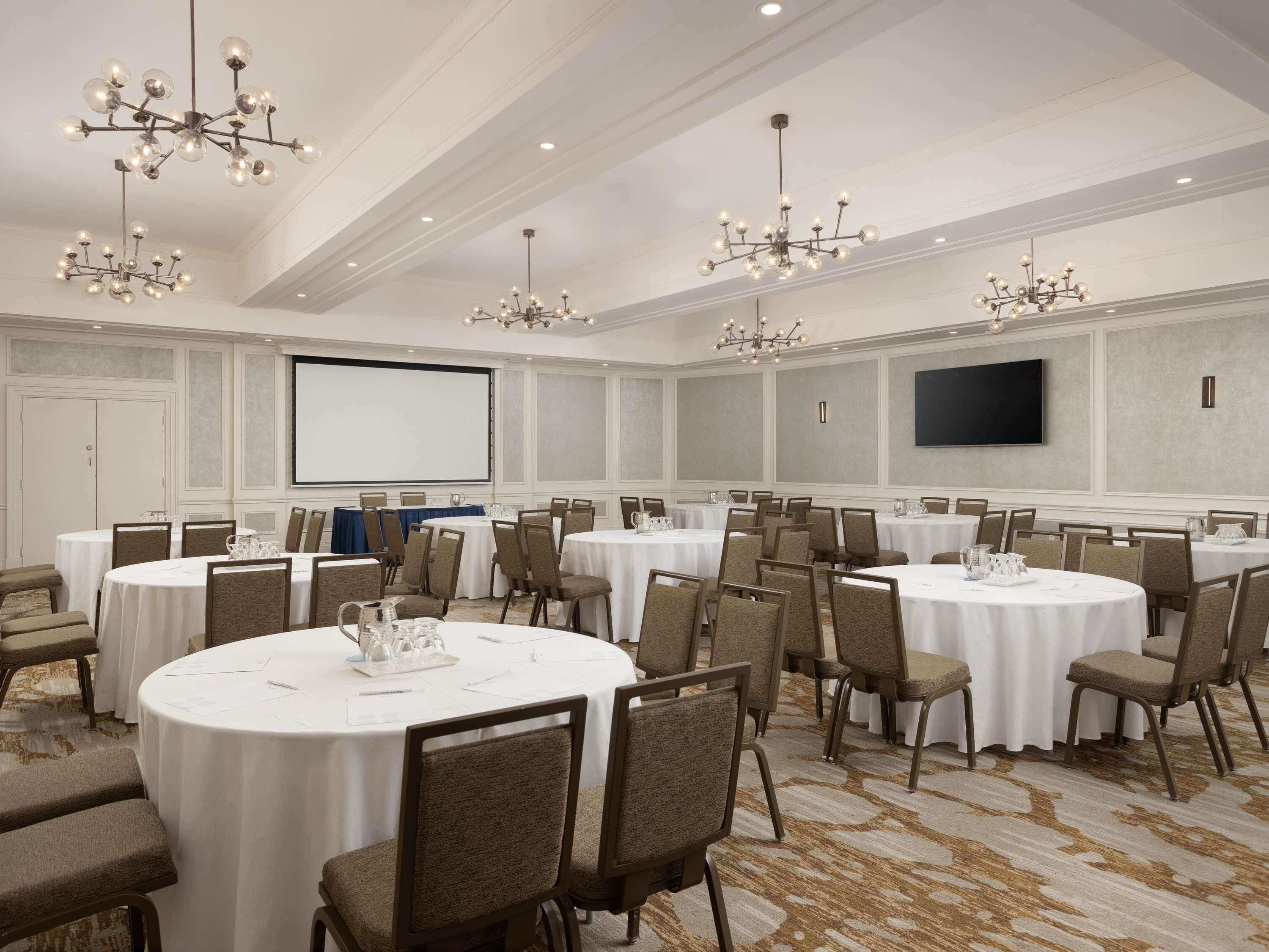 Un salón de conferencias con varias mesas redondas, sillas y candelabros.