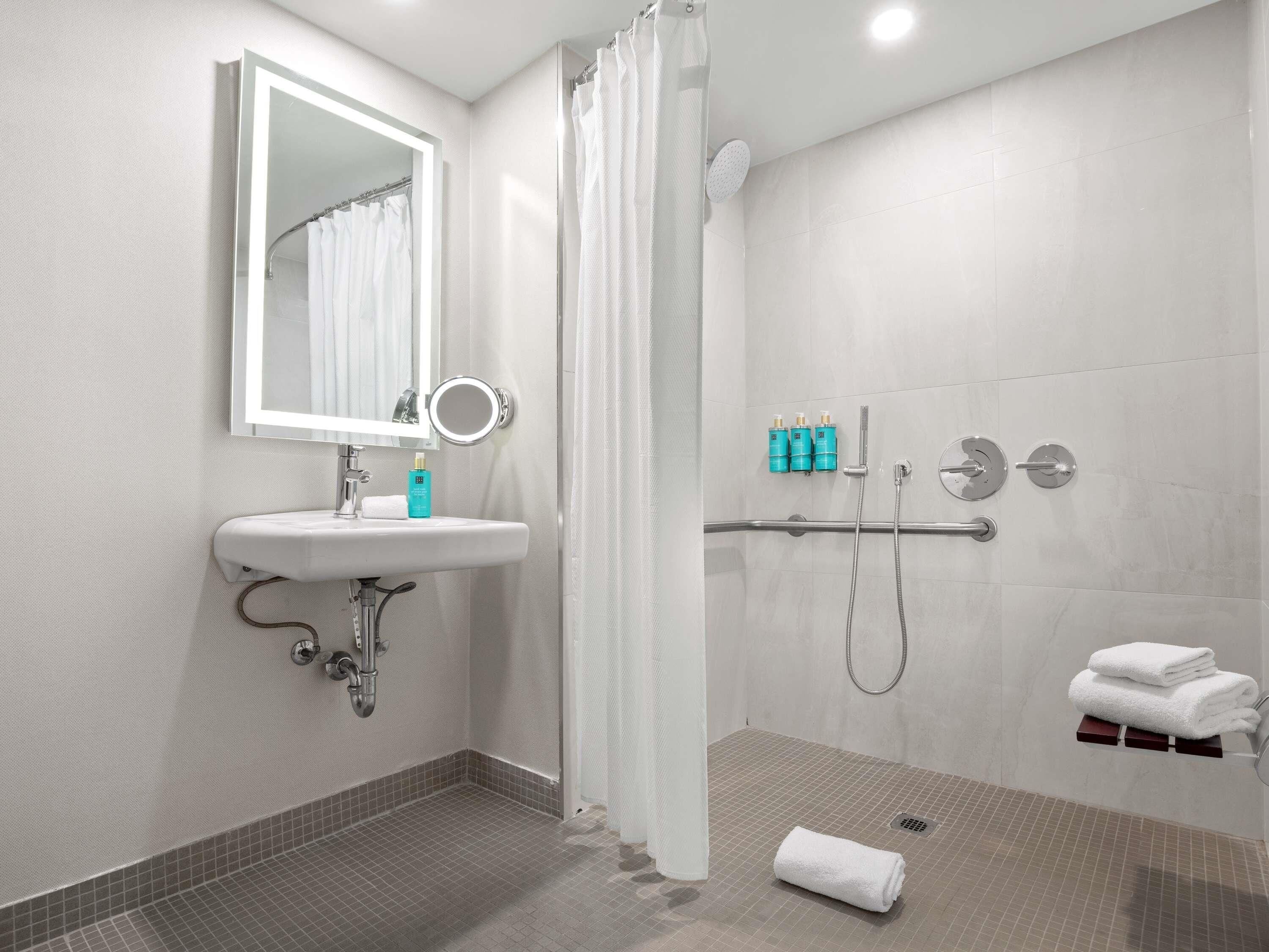 Casa de banho moderna com lavatório, espelho, chuveiro e suporte para toalhas.